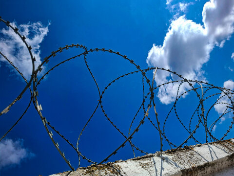 Barbed wire along a fence in front of blue sky with clouds