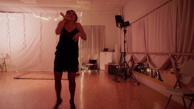 Sexy woman in retro attire with fancy vintage hairstyle dancing alone in low-light hall, performing elegant dance movements with cheerful expressive energy, classic nostalgic style captured. 4K video
