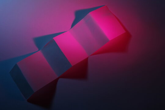 Escultura geom&eacute;trica construida con cart&oacute;n reciclado formando una escalera ascendente, con iluminaci&oacute;n vibrante en tonos magenta y azul que proyecta sombras intensas y suaves.