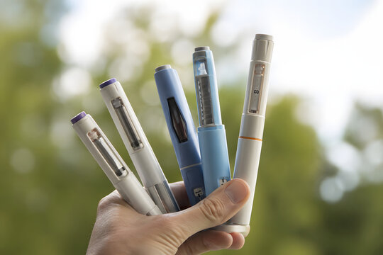 Close-up of hand holding multiple modern injection pens fanned out, symbolizing advanced treatment options, precision medicine and patient choice in contemporary healthcare.

