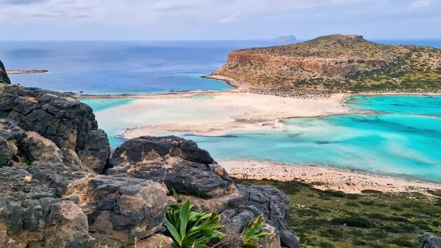 Greece Crete 4K Panning Video of Balos Lagoon and Gramvousa Island from Rocky Cliff with black boulders Green Leaves and Turquoise Sea Scenic Mediterranean Landscape Travel