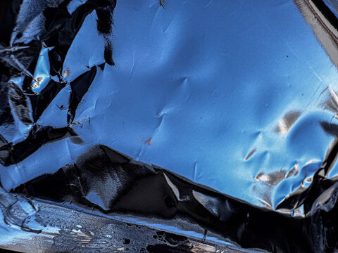 Close up of crumpled blue metallic foil texture with dark reflections, abstract glossy background for industrial packaging and modern design concepts