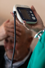 nurse holding digital blood pressure monitor while elderly patient looks worried, home medical care...