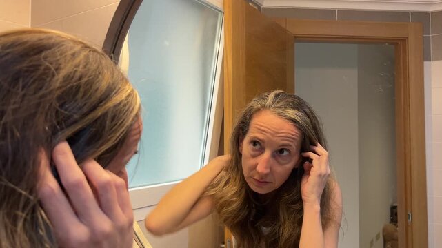 Mujer en menopausia mirando sus canas en el espejo