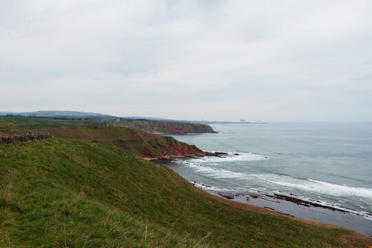 Scenic coastal landscape of Siccar Point with red sandstone cliffs and rocky shoreline in Berwickshire Scotland