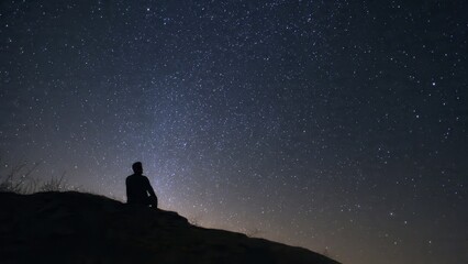 Fototapeta premium Silhouette of Person Sitting on Hill Under Starry Sky