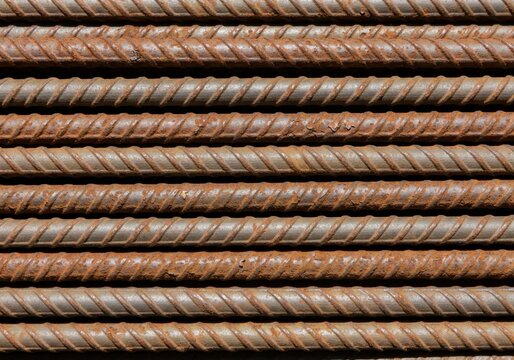 A close-up full-frame shot of multiple rusty rebar rods stacked horizontally, displaying textured metal with corrosion.