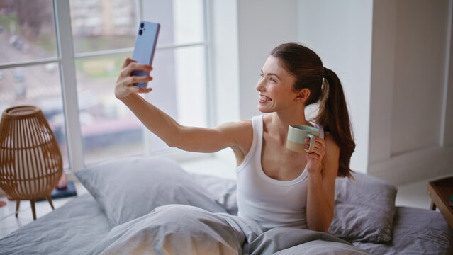 Sensual woman posing mobile phone selfie in morning bed closeup. Modern female
