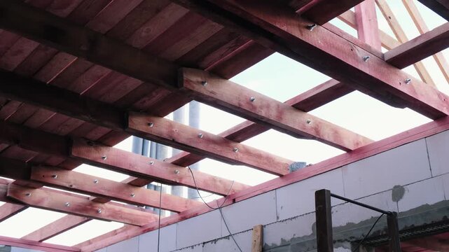 Upward moving shot of wooden roof beams inside unfinished house, showing structural frame, bolts and open sky, ideal for construction, carpentry, building process and architecture footage
