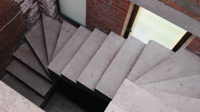 Top view of unfinished concrete staircase inside residential construction site with brick walls and window openings, highlighting building progress, structural work and interior architecture
