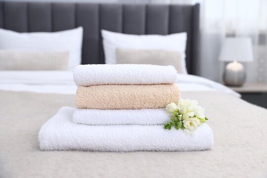 Fresh towels and beautiful freesia flowers on bed indoors, closeup