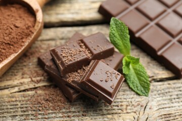 Pieces of yummy chocolate, mint leaves and cocoa powder on wooden table, closeup © New Africa