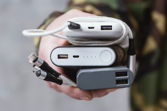 Hand holding multiple power banks with charging cables and connectors for mobile devices. Concept of portable energy, battery backup, gadget accessories and travel technology.