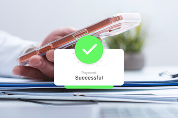 Hand holding a phone with a green payment successful notification pop up over a laptop. Concept for...