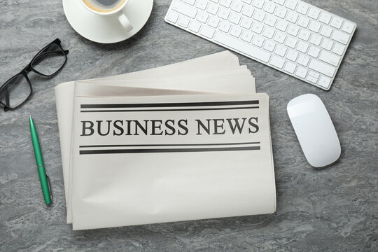 Newspaper, computer keyboard, mouse, pen, glasses and coffee on grey table, flat lay