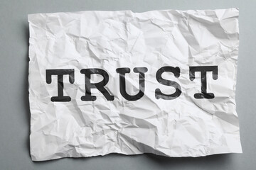 Naklejka premium Crumpled paper with word Trust on grey background, top view. Betrayal