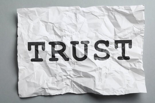 Crumpled paper with word Trust on grey background, top view. Betrayal