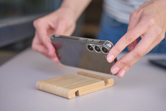 Hands place smartphone on wooden stand on kitchen counter