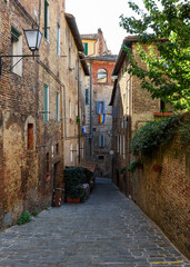 Obraz premium Medieval narrow street with tables of restaurant in Siena, Tuscany, Italy. Architecture and landmark of Siena. Cozy cityscape of Siena