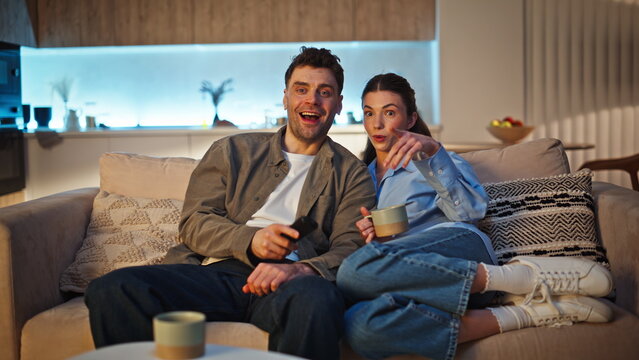 Relaxed lovers watching movie switching channels at late home. Couple looking tv