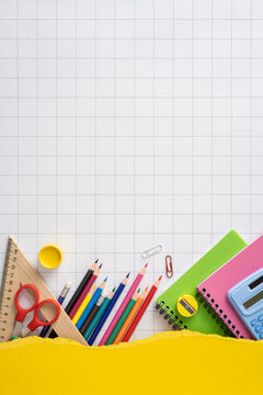 Back to school vertical flat lay with colorful pencils scissors ruler notebooks and calculator on grid background