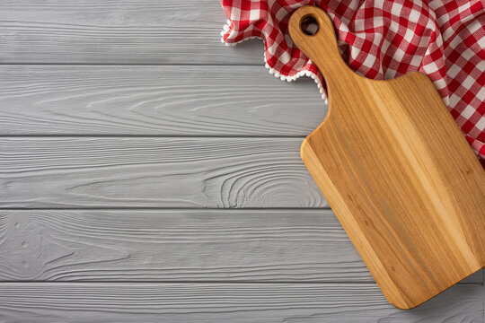 Wooden cutting board and red checkered cloth on gray table for kitchen preparation and cooking