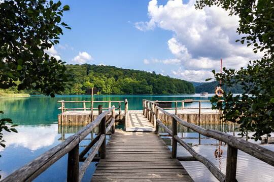 Scenic wooden pier clear turquoise lake toward ferry boat passengers green forest Plitvice lakes national park. Calm water reflections sunlight peaceful summer travel scene summer Croatia sightseeing