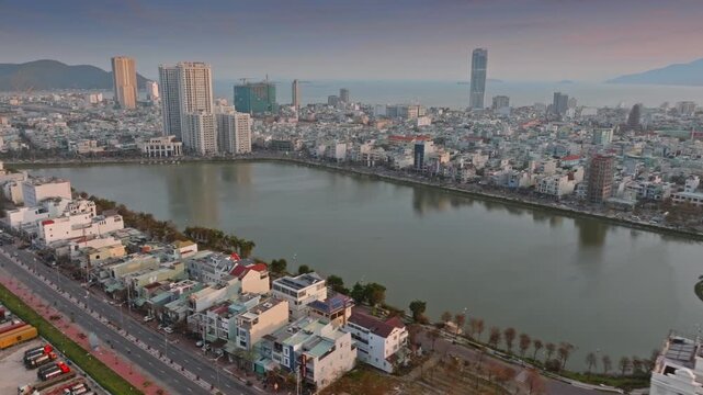 Aerial view of  Quy Nhon, Binh Dinh, Vietnam, with its modern skyline, a tranquil Ho Sinh Thai lake, and mountains in the background at sunset.