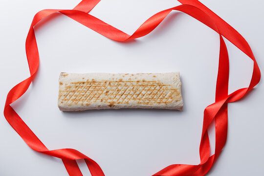 Grilled wrap shaverma with red ribbon on white background in heart shape, top view
