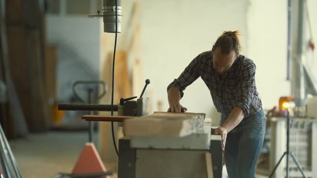 Carpenter using jointer plane machine in workshop