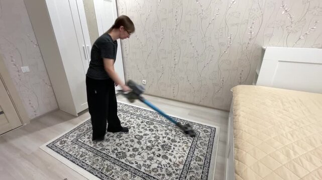 Female vacuuming patterned area. Woman maintains decorative rug in contemporary bedroom environment. Female individual thoroughly cleans and organizes stylish carpet within modern bedroom setting
