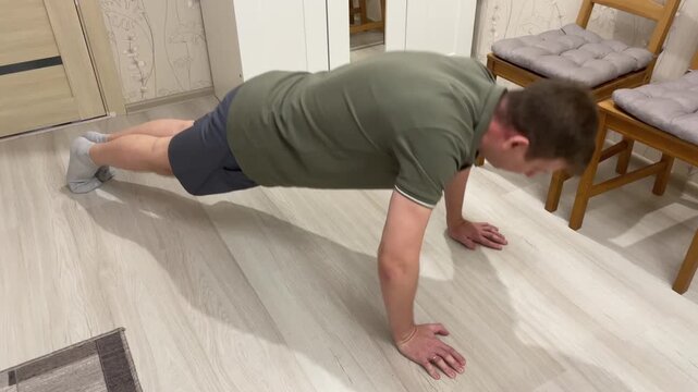Men executing controlled pushups indoors. Male performing plank and pushup exercises indoors. Man carefully transitioning through various pushup styles on wooden floor for strength and stamina