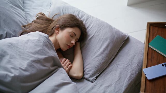 Tired woman reacting alarm smartphone lying at home bed continue sleep closeup