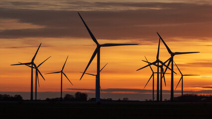 Fototapeta premium Windräder in einem Windpark bei Struckum nahe der Nordsee in Nordfriesland, Schleswig-Holstein, Deutschland bei Sonnenuntergang.