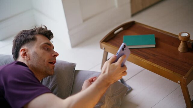 Rested brunette checking alarm cellphone lying comfortable home pillows closeup