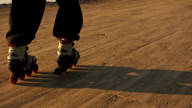 Low angle rear view of orange-wheeled inline skates gliding on warm golden wooden promenade. Long dramatic wheel shadows, motion blur, sunset light. Active summer sport, speed and freedom.
