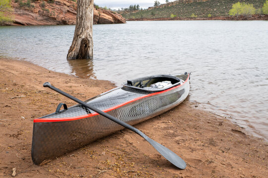 decked touring canoe with carbon fiber hull and rudder at a shore of calm lake