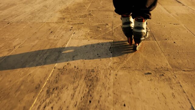 Low angle rear view of inline skates gliding on golden lit wooden promenade. Long shadows, warm sunset light, textured deck. Active sport, skating and summer freedom concept.

