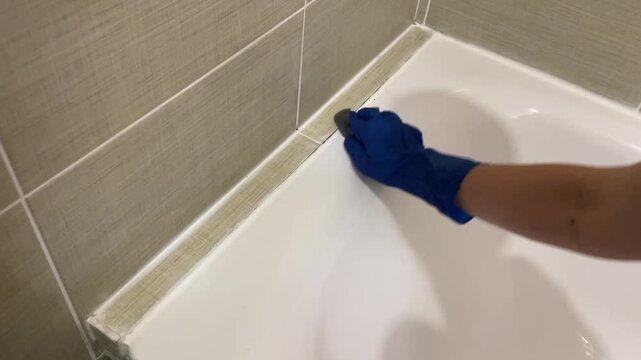 Cleaning reveals shine, Scrubbing removes dirt effectively, Gloved hands meticulously scrub tile joints thoroughly, Diligent cleaning with sponge uncovers pristine surfaces and clear grout lines
