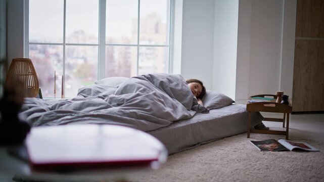 Lazy woman sleeping mattress checking time on mobile phone. Brunette waking up
