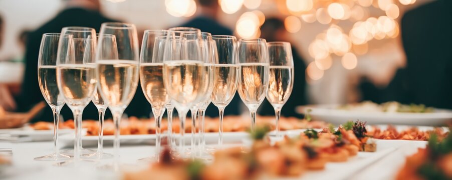 Elegant buffet table with champagne glasses and delicate hors d'oeuvres, bathed in warm cinematic lighting. The soft bokeh and vibrant atmosphere evoke a luxurious celebration.