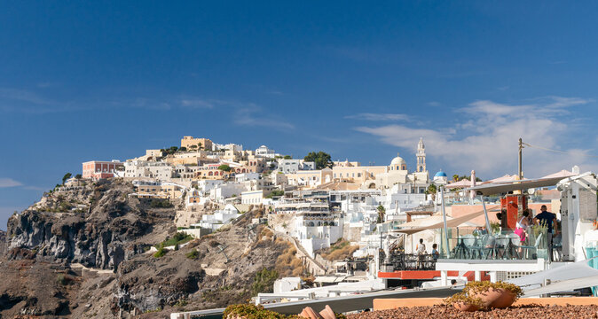 Panor&aacute;mica de Fira en Santorini, Grecia, con sus ic&oacute;nicas casas blancas escalonadas sobre el acantilado volc&aacute;nico frente al mar Egeo bajo un cielo azul despejado.
