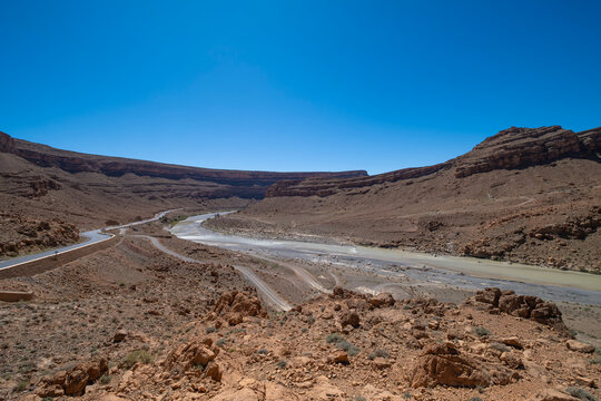 Desert canyon with winding river and road cutting through rocky terrain under clear blue sky remote arid landscape with dramatic geology and vast open space, Ziz river in the Middle Atlas mountains