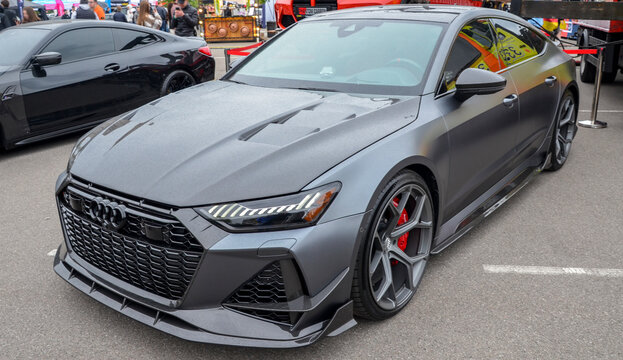 Matte grey Audi RS7 with an aggressive widebody kit and red brake calipers at car show. A high performance German sportback icon