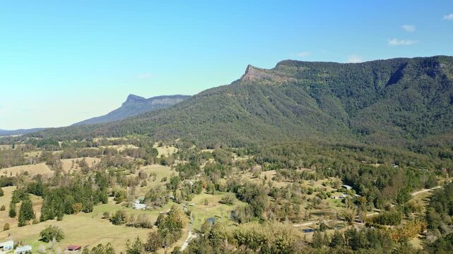 Large peaky mountain sticking out of mountain range with farms in valley below.