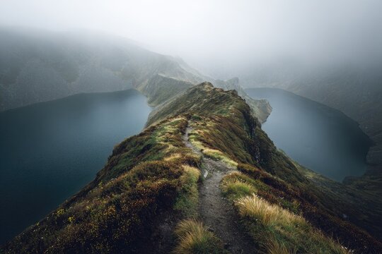 Narrow, grassy ridge separates dark lakes under misty sky