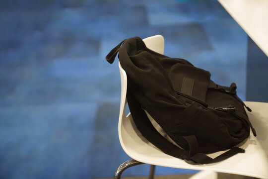 Black Backpack on White Chair on Blue Minimal Background