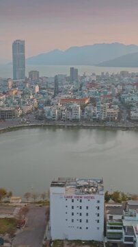 Aerial view of  Quy Nhon, Binh Dinh, Vietnam, with its modern skyline, a tranquil Ho Sinh Thai lake, and mountains in the background at sunset.