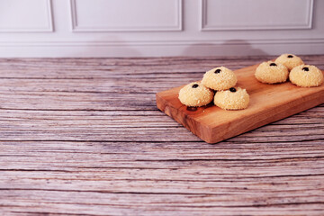 Fototapeta premium Kue Monde Susu or cookies rest on a rustic wooden board. Each cookie has a small choco chip on top. The board rests on weathered wood, adding warmth to the scene. Ideal for cozy cafe or home baking 