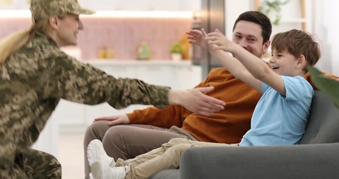 Soldier coming home. Woman i military uniform hugging her family on sofa indoors